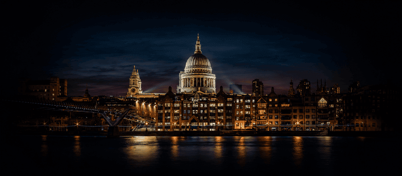 A river skyline at dusk with a domed landmark building lit against the evening sky.